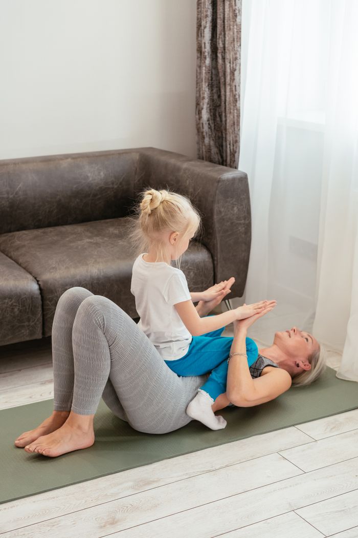 About A grandmother and her granddaughter enjoy a playful exercise session on a yoga mat indoors.