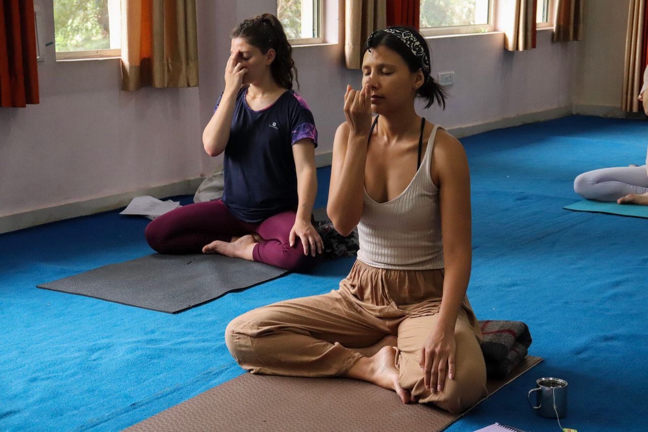 Menus Two women practicing yoga breathing exercises indoors in Rishikesh, India.
